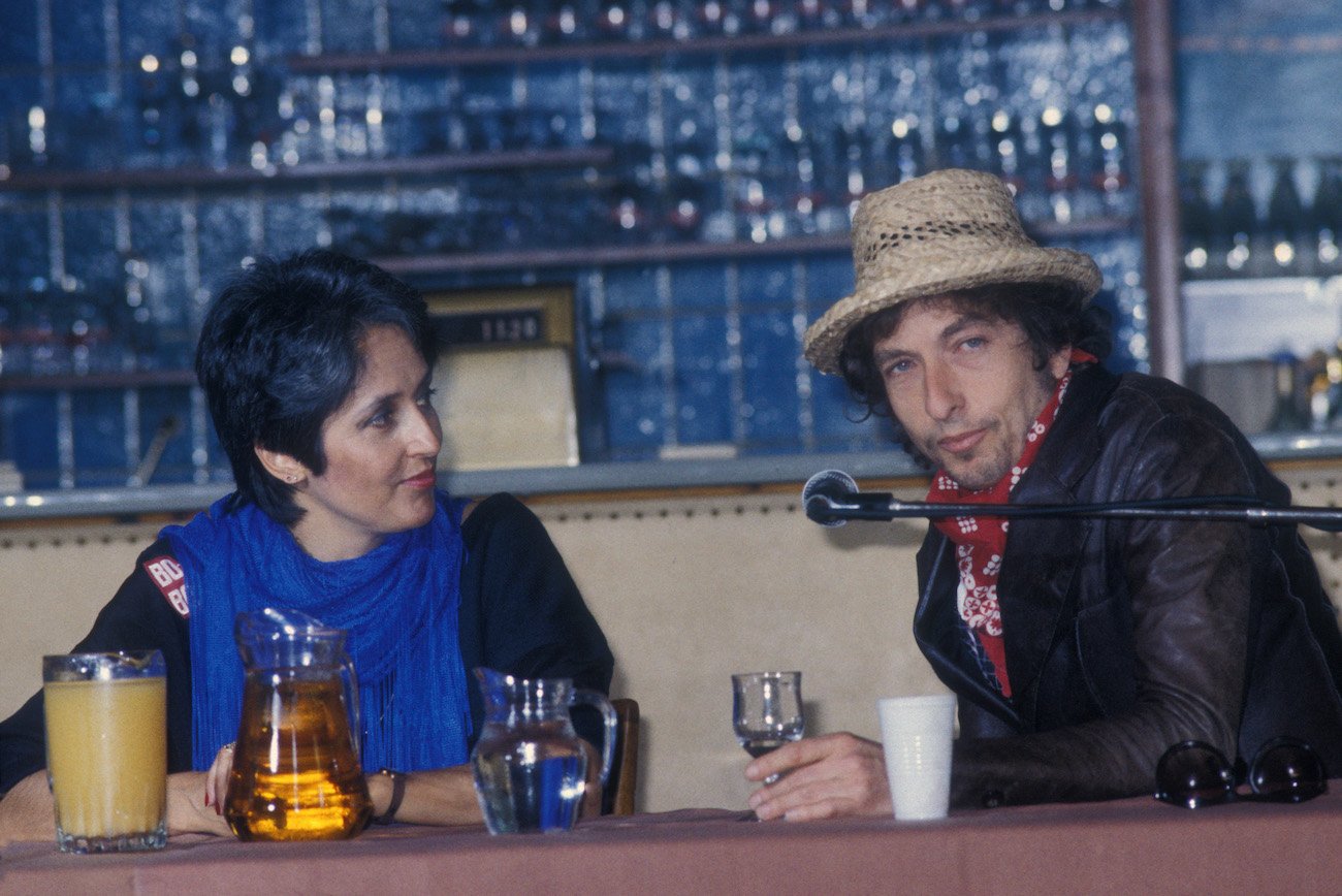 Joan Baez in black and blue with Bob Dylan dressed in a brown leather jacket during a press conference in Germany, 1984.