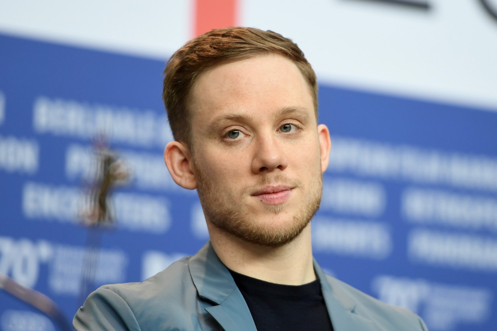 A close-up of Joe Cole's face against a blue background, the actor who plays John Shelby in 'Peaky Blinders