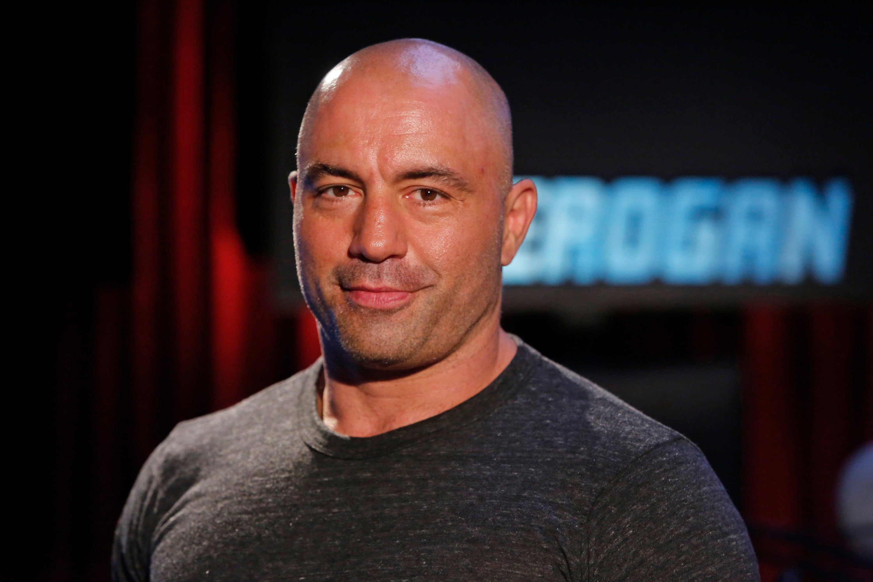 Joe Rogan wears a black shirt and poses for a photo.
