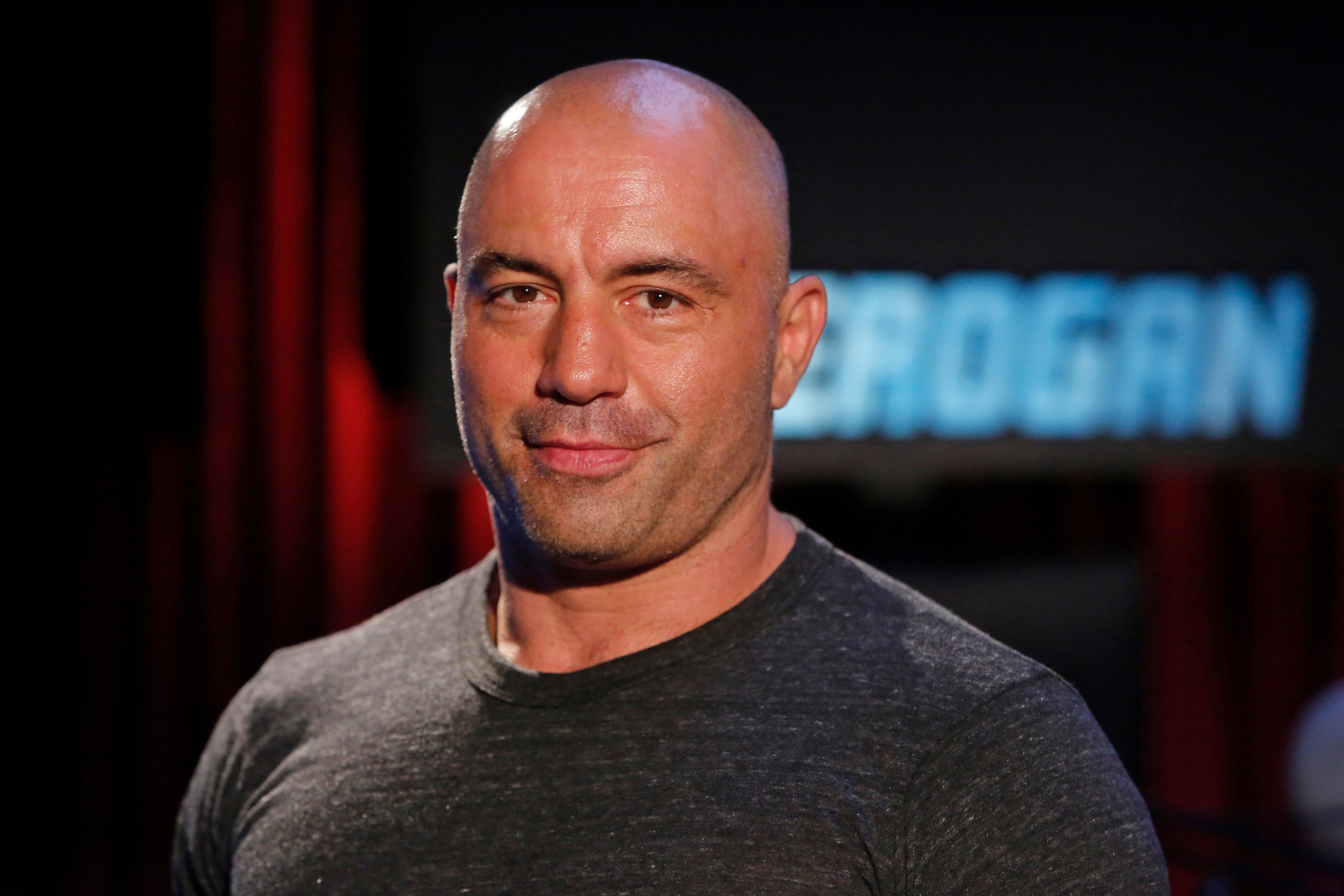 Joe Rogan wears a black shirt and poses for a photo.