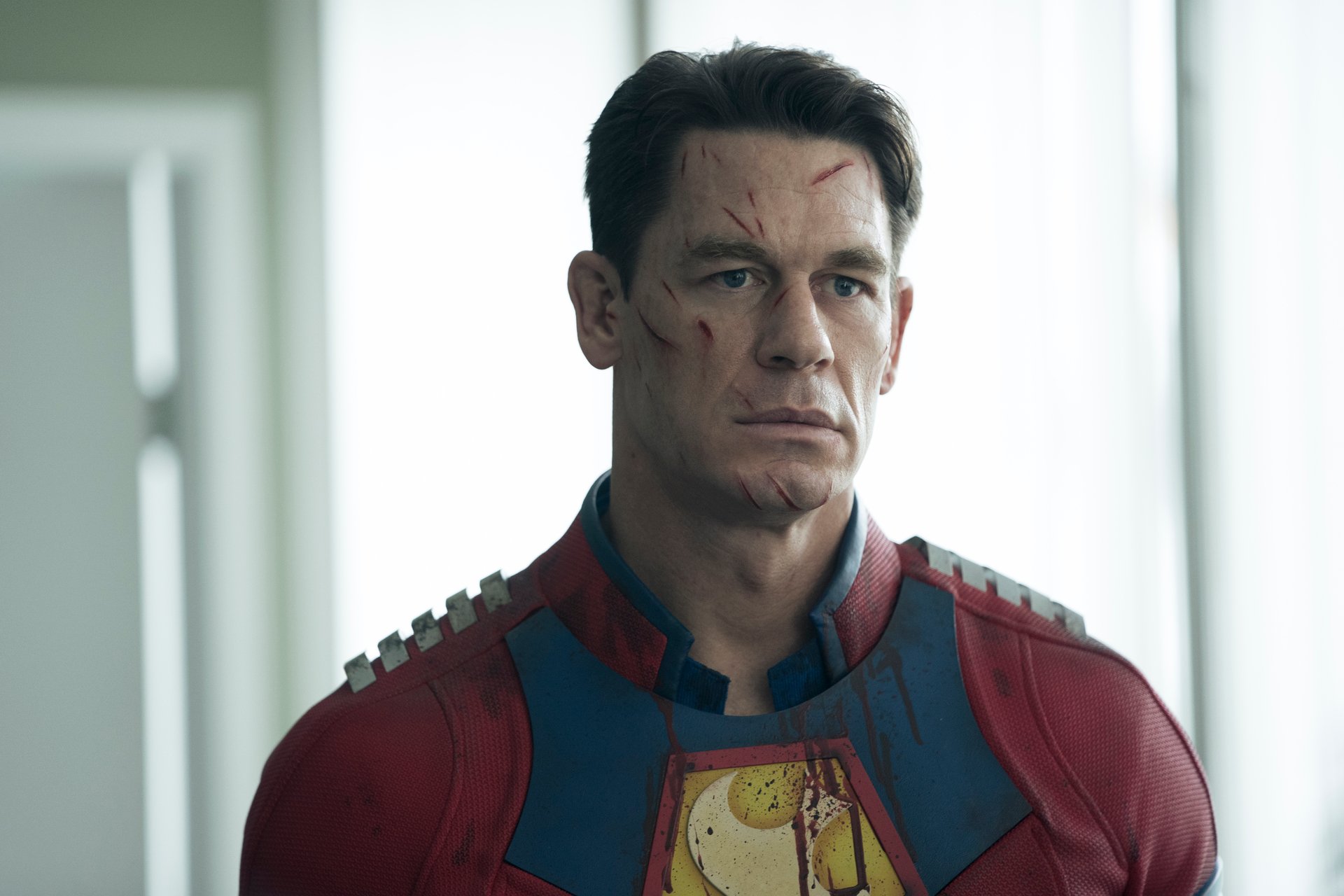 John Cena as Christopher Smith in DC's 'Peacemaker.' His face has a number of cuts on it, and he looks grim.