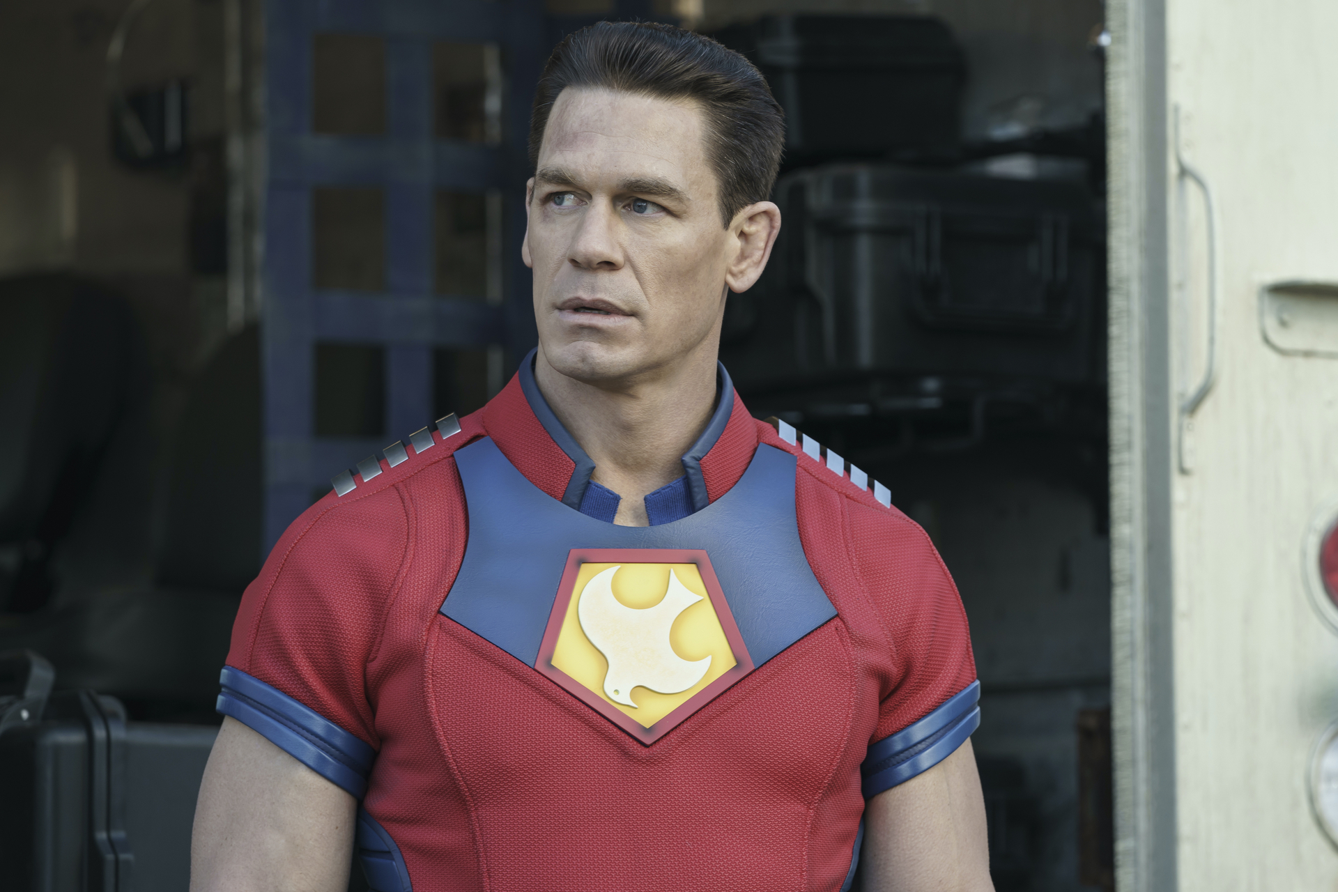 John Cena in episode 3 of DC's 'Peacemaker.' He's wearing his red, yellow, and blue suit and looking to the side.