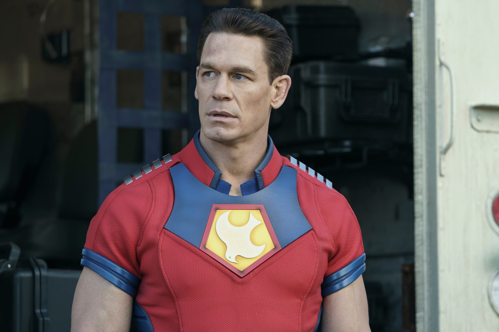 John Cena in episode 3 of DC's 'Peacemaker.' He's wearing his red, yellow, and blue suit and looking to the side.