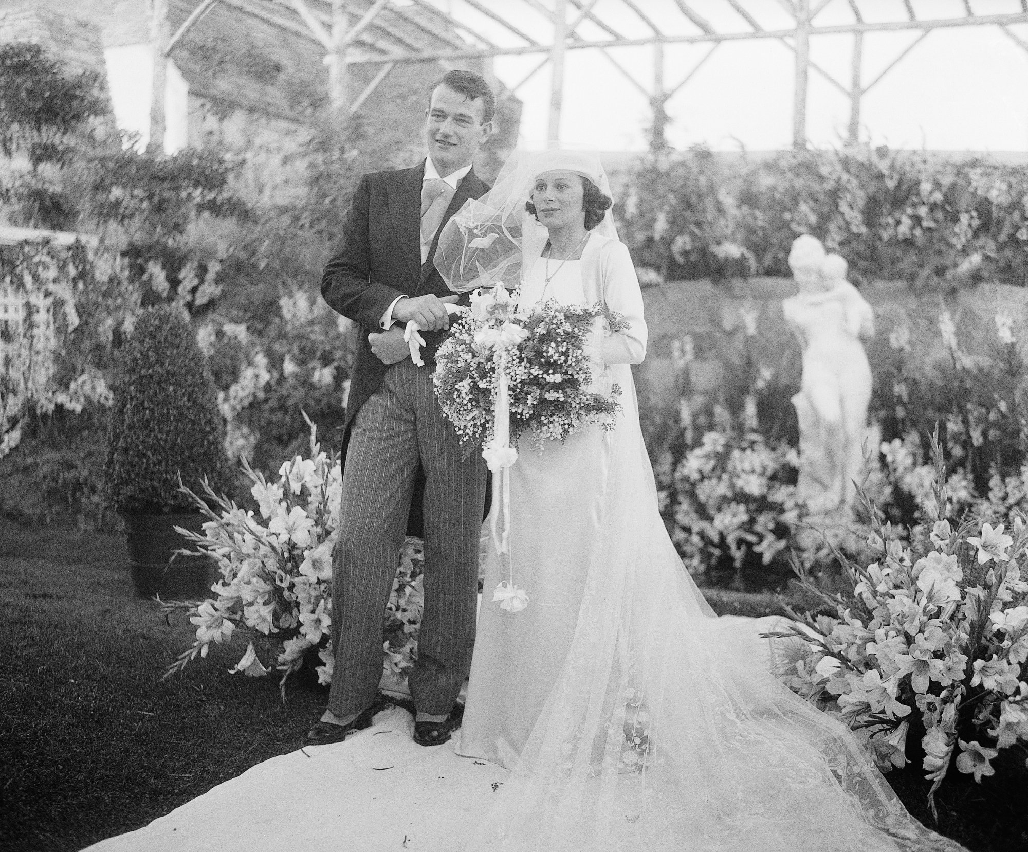 John Wayne and wife Josephine Saenz in wedding attire in front of flowers
