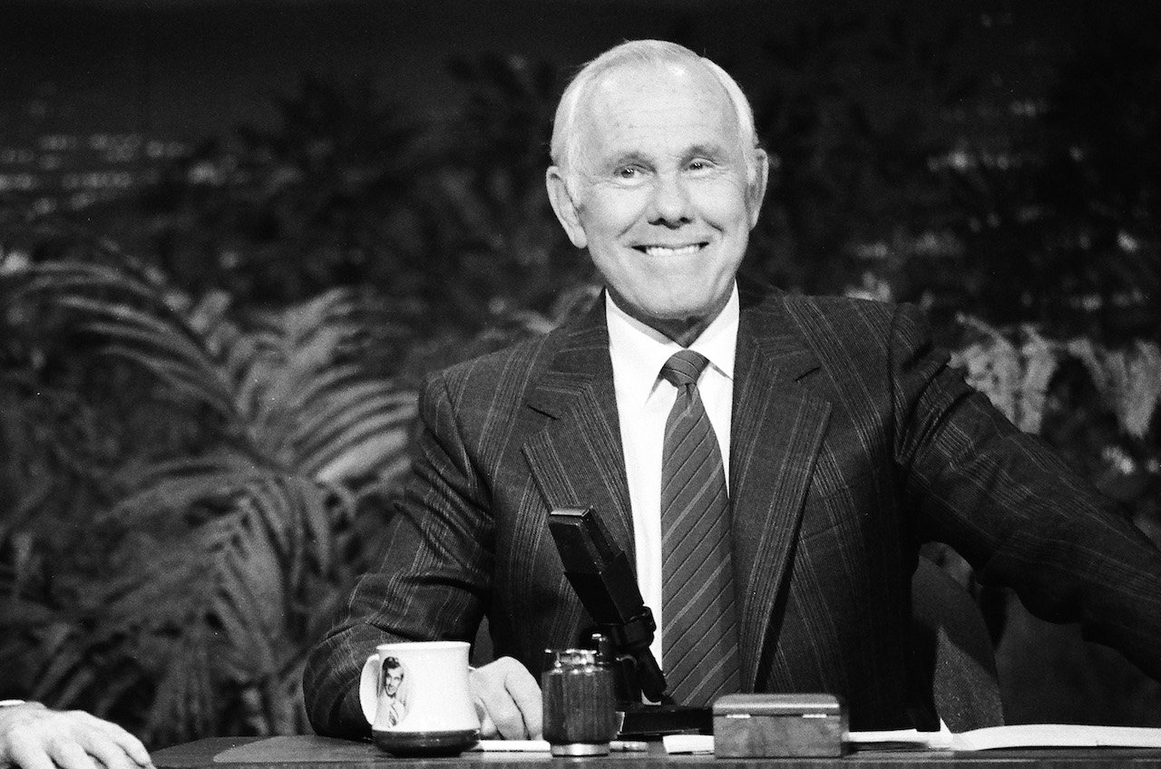 Black and white photo of Johnny Carson in a suit behind 'The Tonight Show' desk