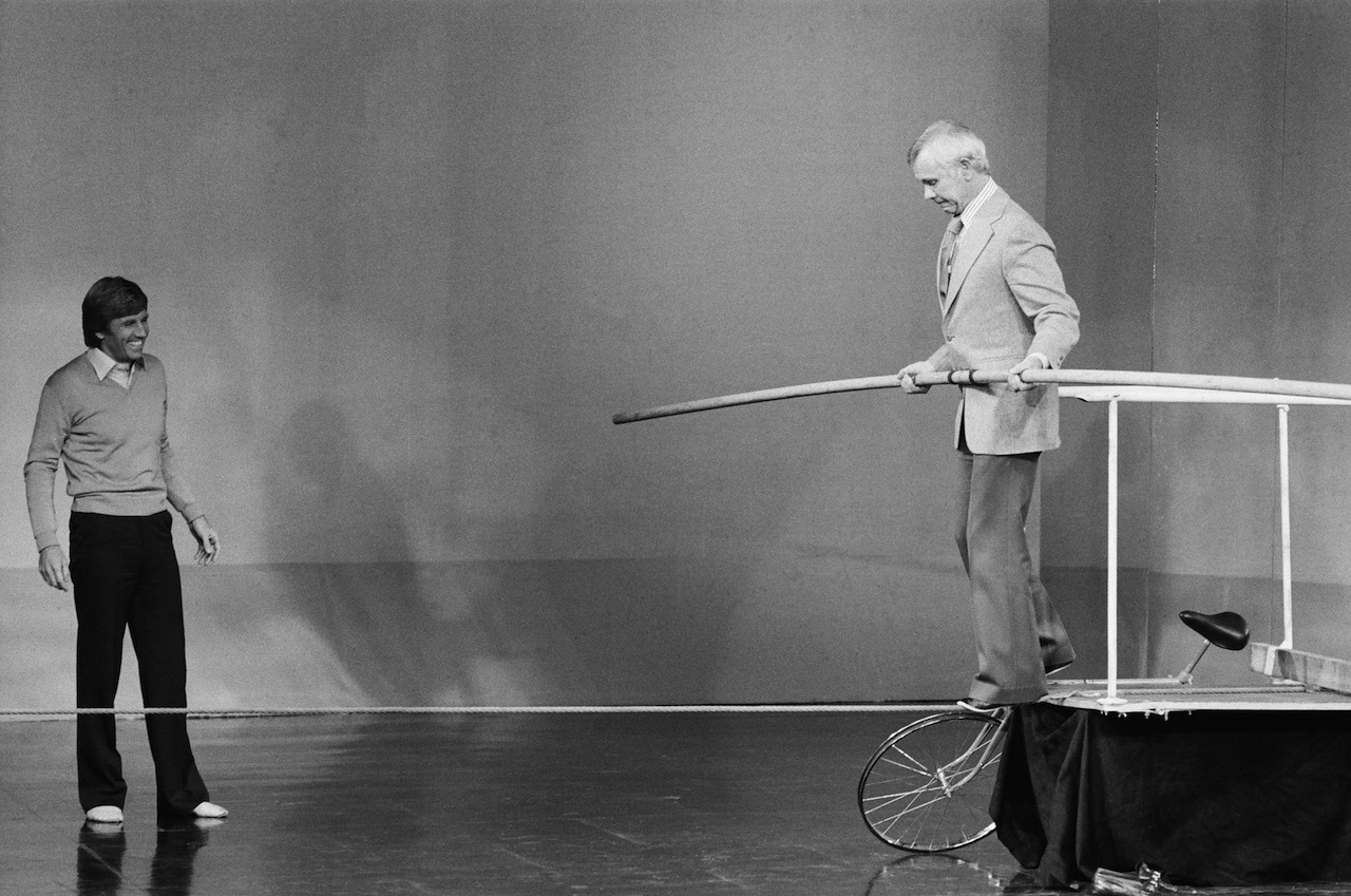 (l-r) Actor Gary Collins watches as Johnny Carson walks on a tightrope