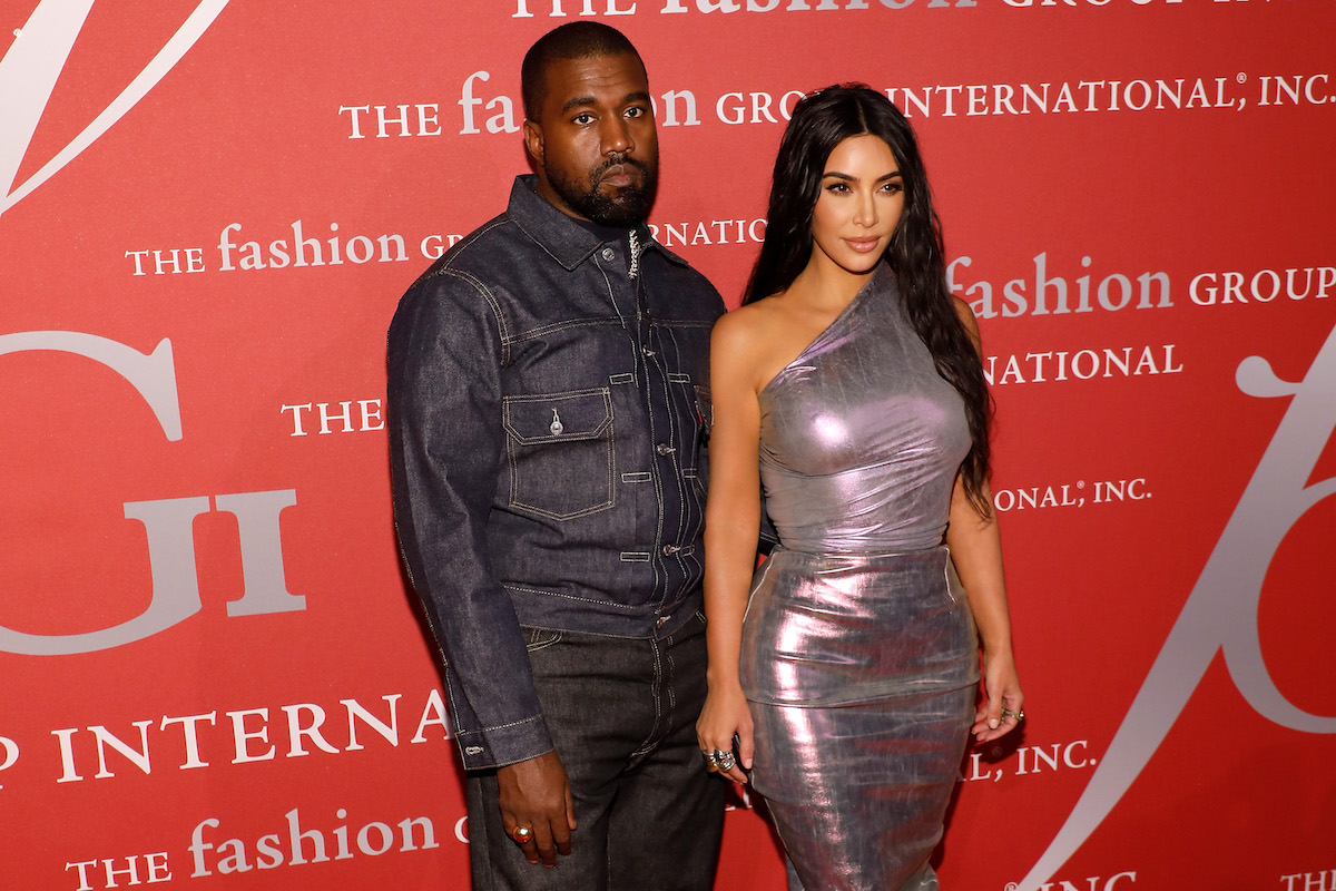 Kanye West wearing a denim jacket and Kim Kardashian West wearing a metallic dress pose together at an event.