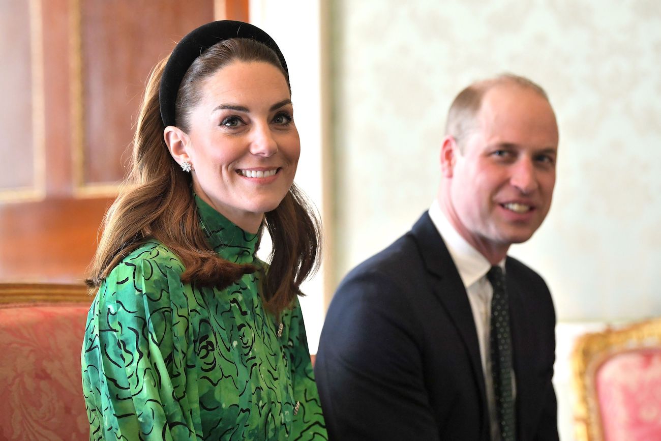 Kate Middleton wearing a green outfit and a headband, with Prince William wearing a suit in the background