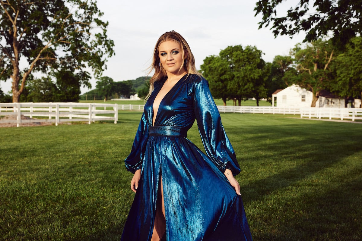 Country singer Kelsea Ballerini wears a shiny blue dress while posing on a farm in Nashville, Tennesse