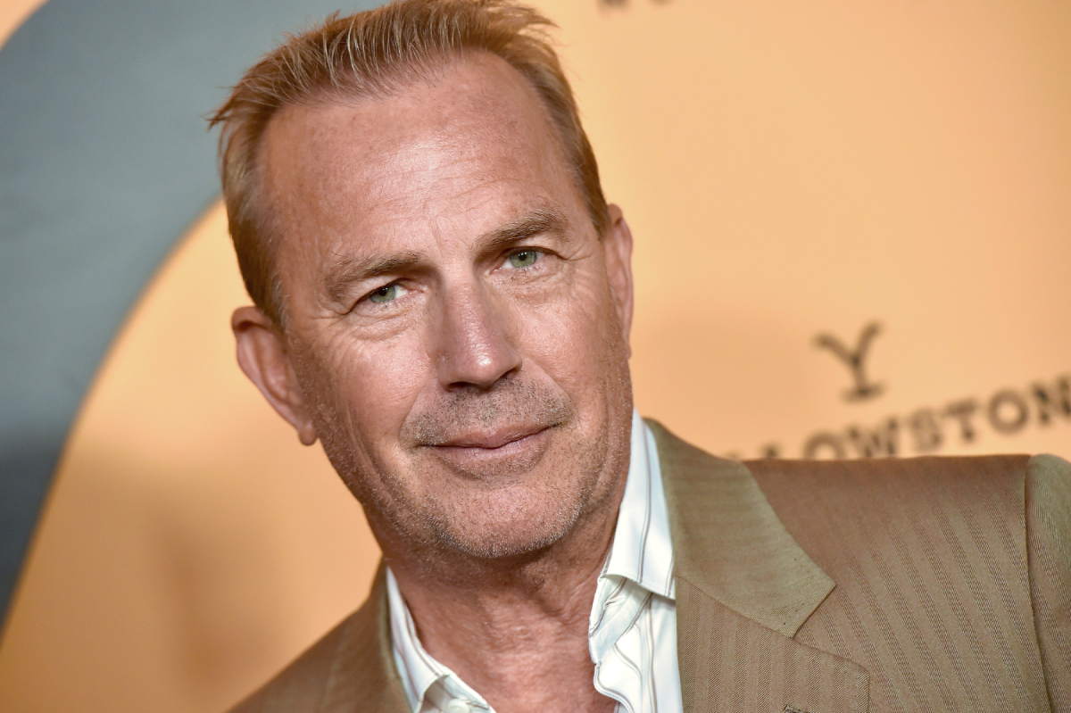 Kevin Costner pictured wearing a brown suit jacket and white shirt and shot from the shoulders up at the premiere of Yellowstone season 2