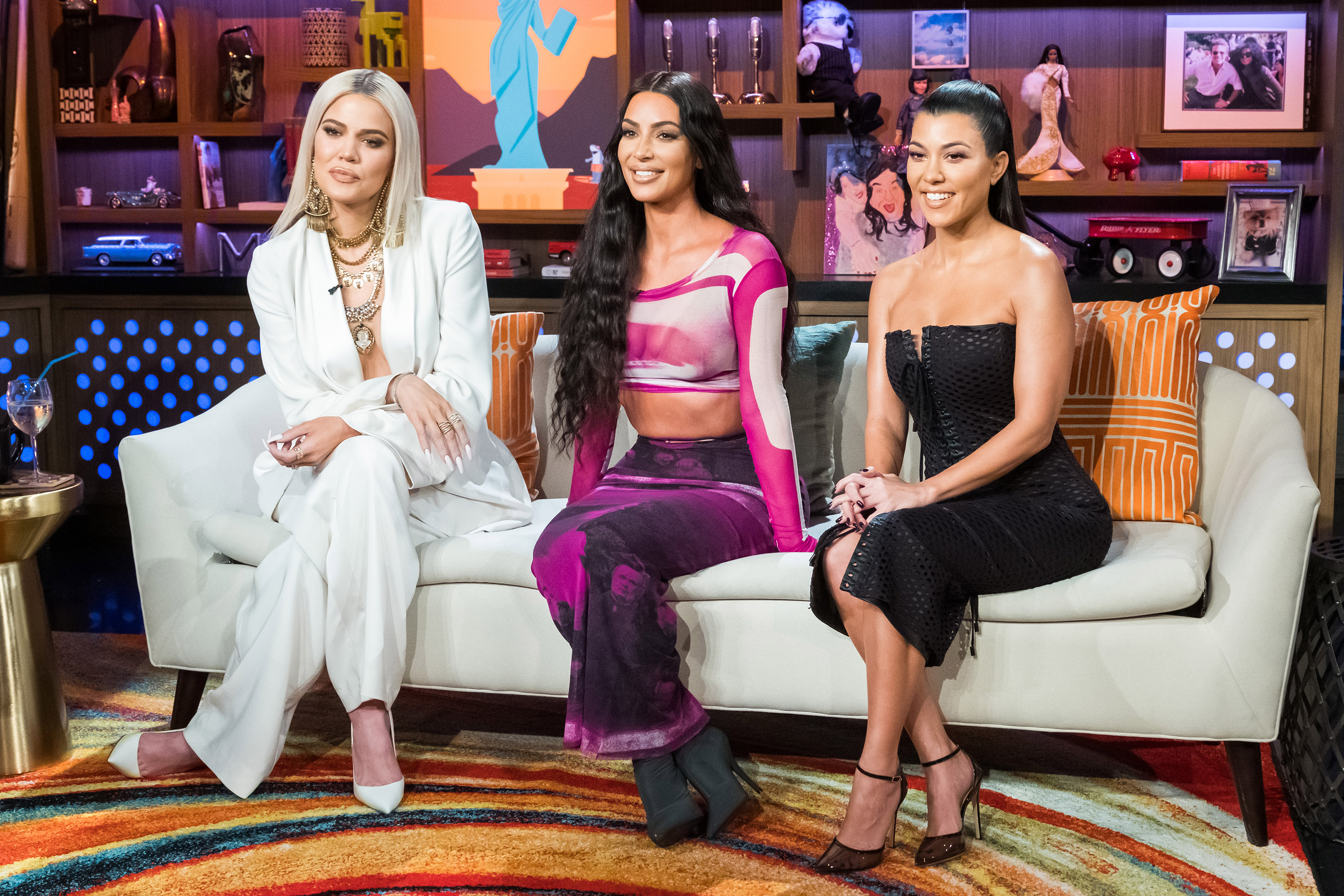 Khloe Kardashian, Kim Kardashian, and Kourtney Kardashian sitting on a white couch and looking on