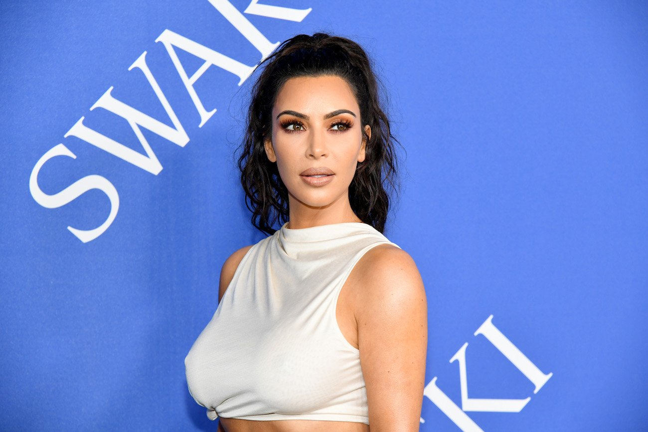 Kim Kardashian West wearing white, looking on in front of a blue background