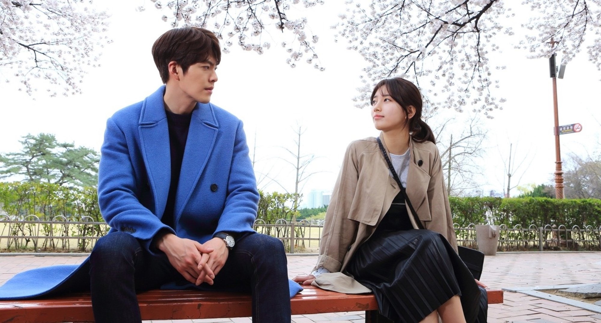Kim Woo-bin and Bae Suzy for 'Uncontrollably Fond' Valentine's Day romance K-drama sitting on bench outside.