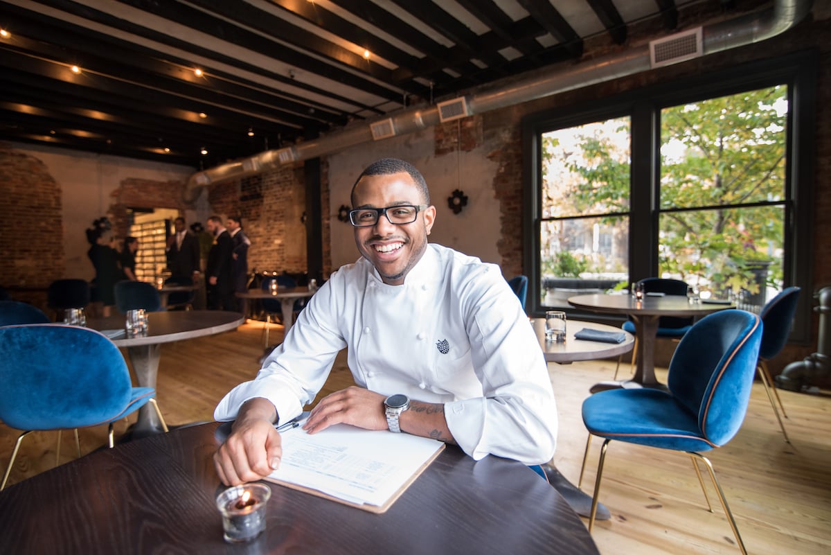 Kwame Onwuachi poses at a table in a restaurant.