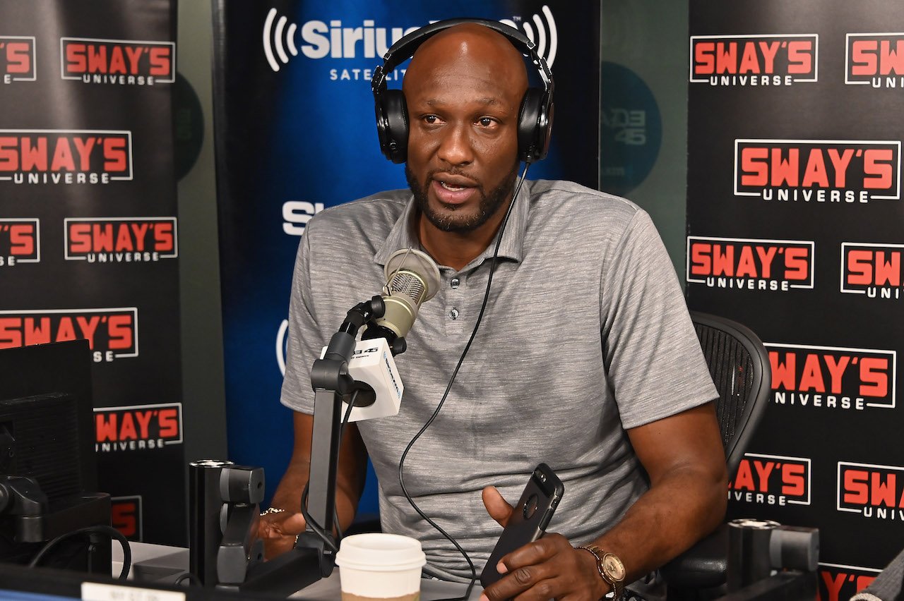 Lamar Odom sits in front of a microphone talking as he wears headphones.