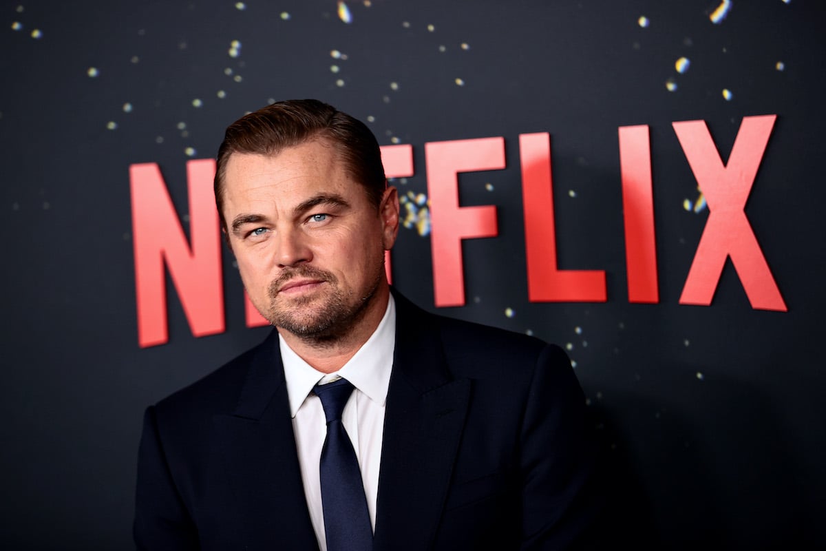 Leonardo DiCaprio wears a suit and poses in front of the Netflix logo