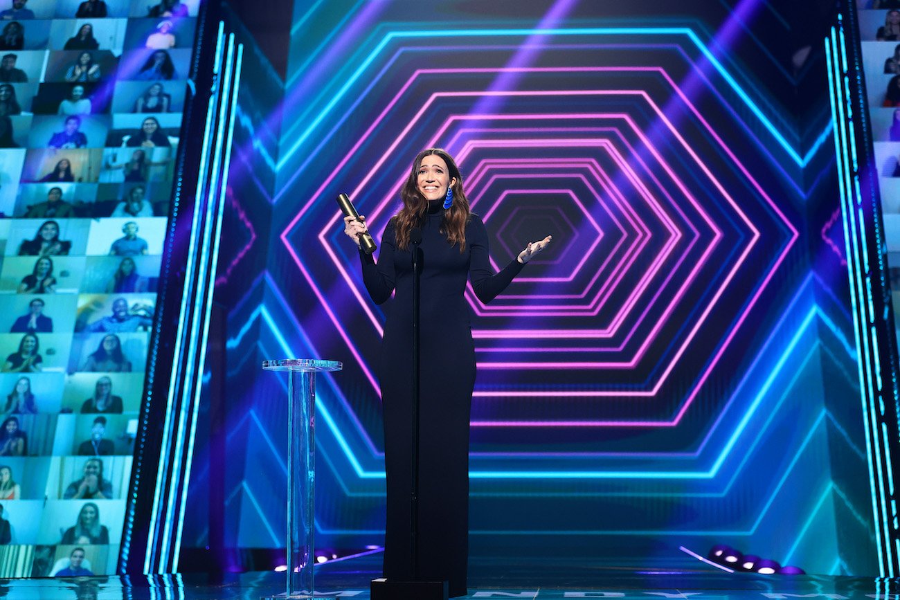 Mandy Moore holds an awards and speaks into a microphone wearing a black gown