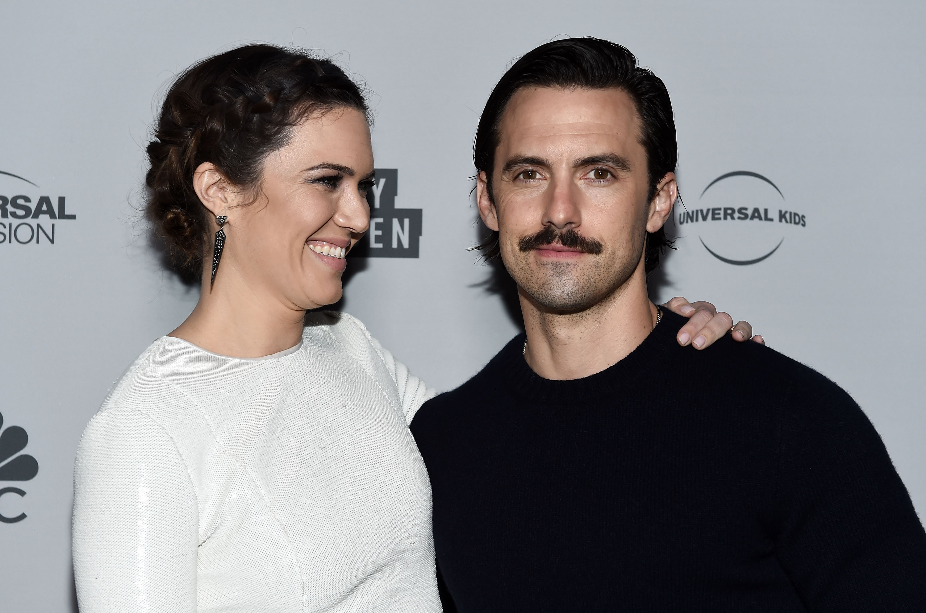 Mandy Moore and Milo Ventimiglia pose for pictures together. Moore wears a white dress. Venitmiglia wears a black shirt.