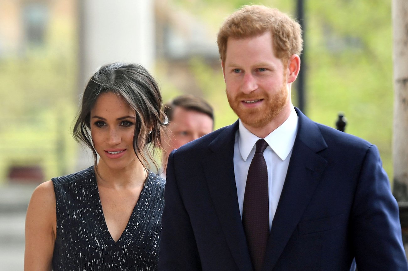 Meghan Markle wearing a sleeveless dress and Prince Harry wearing a suit