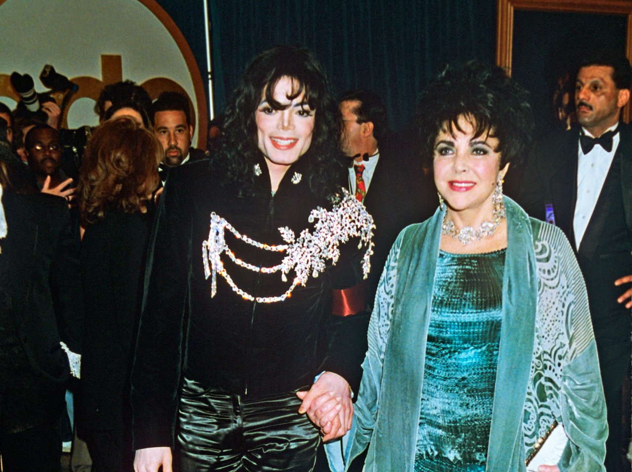 Michael Jackson in a black top with diamond adornments, standing next to Elizabeth Taylor in teal and diamonds