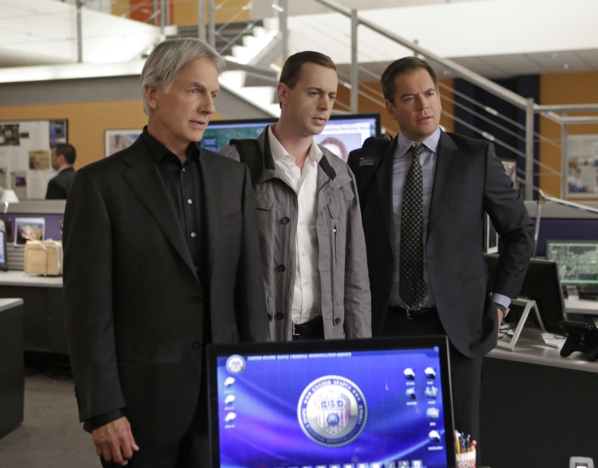 Mark Harmon, Sean Murray, and Michael Weatherly stand in the office on the set of 'NCIS.'