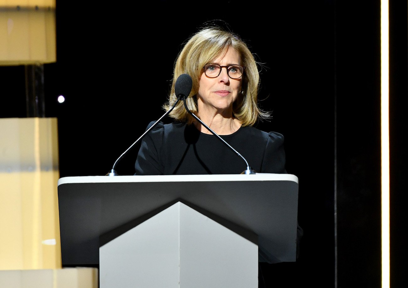 Nancy Meyers stands at a lectern wearing a black shirt and glasses