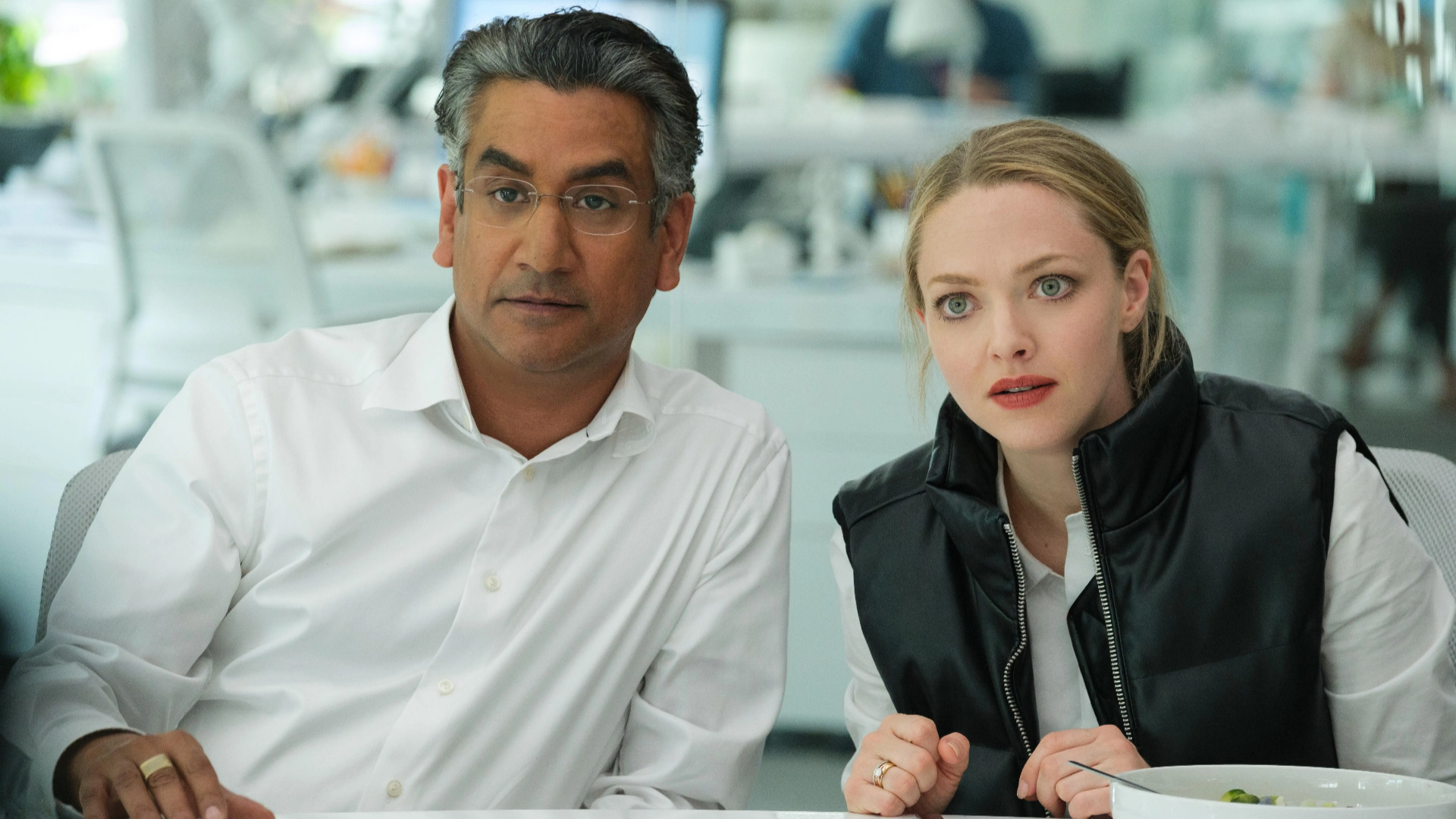 Naveen Andrews as Sunny Balwani and Amanda Seyfried as Elizabeth Holmes sitting together and looking surprised in Hulu’s ‘The Dropout’