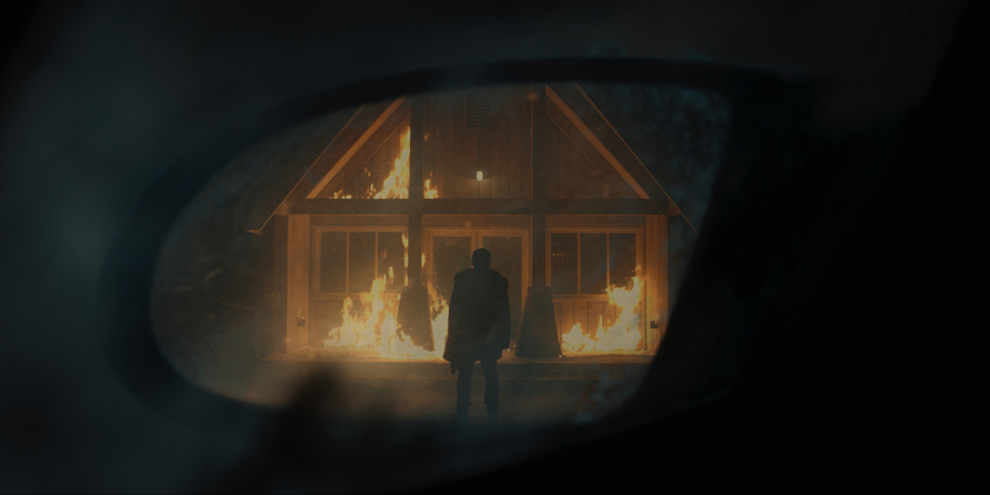 'No Exit' silhouette standing in front of a burning building as seen through a car side mirror
