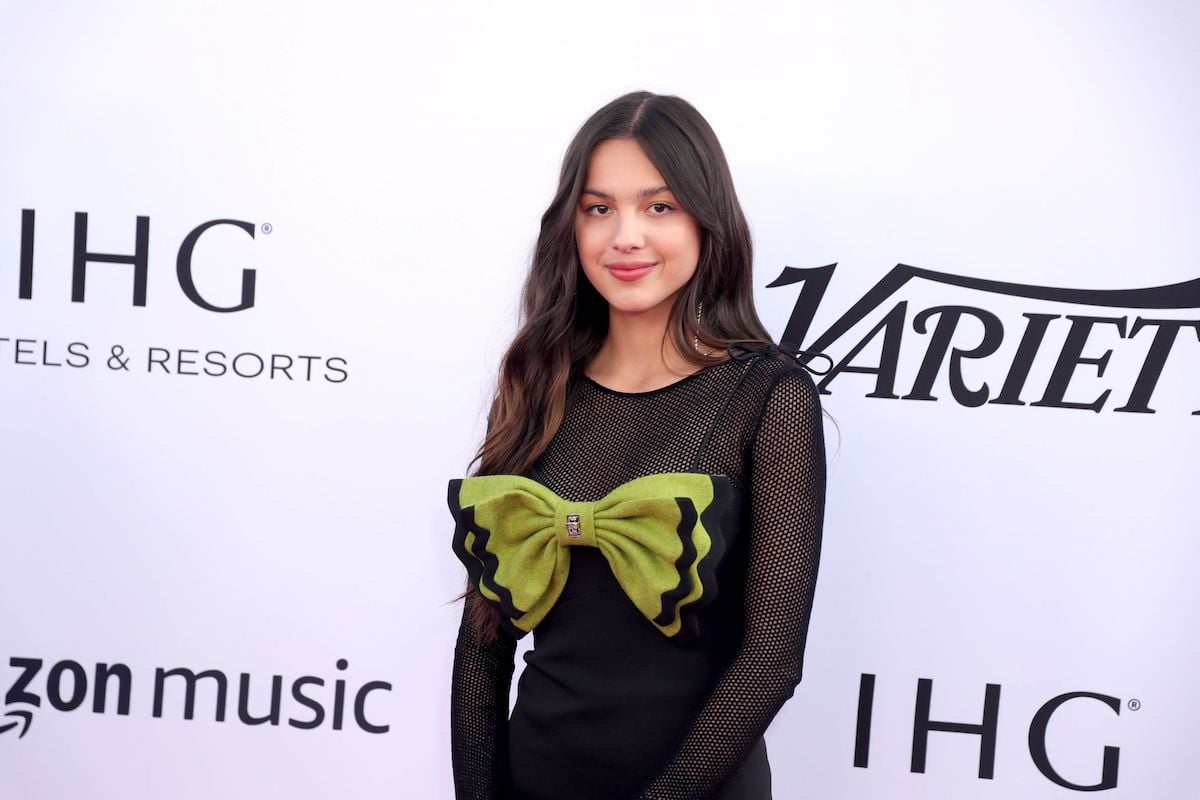 Olivia Rodrigo poses in a black dress with a large green bow at an event.