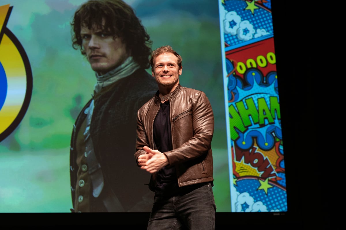 Outlander Sam Heughan -- with a picture of Jamie Fraser behind him -- speaks on stage during Wizard World Comic Con at Ernest N. Morial Convention Center on January 04, 2020