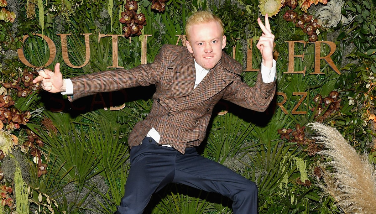 Outlander star John Bell jumps and mugs for the camera in a plaid jacket
