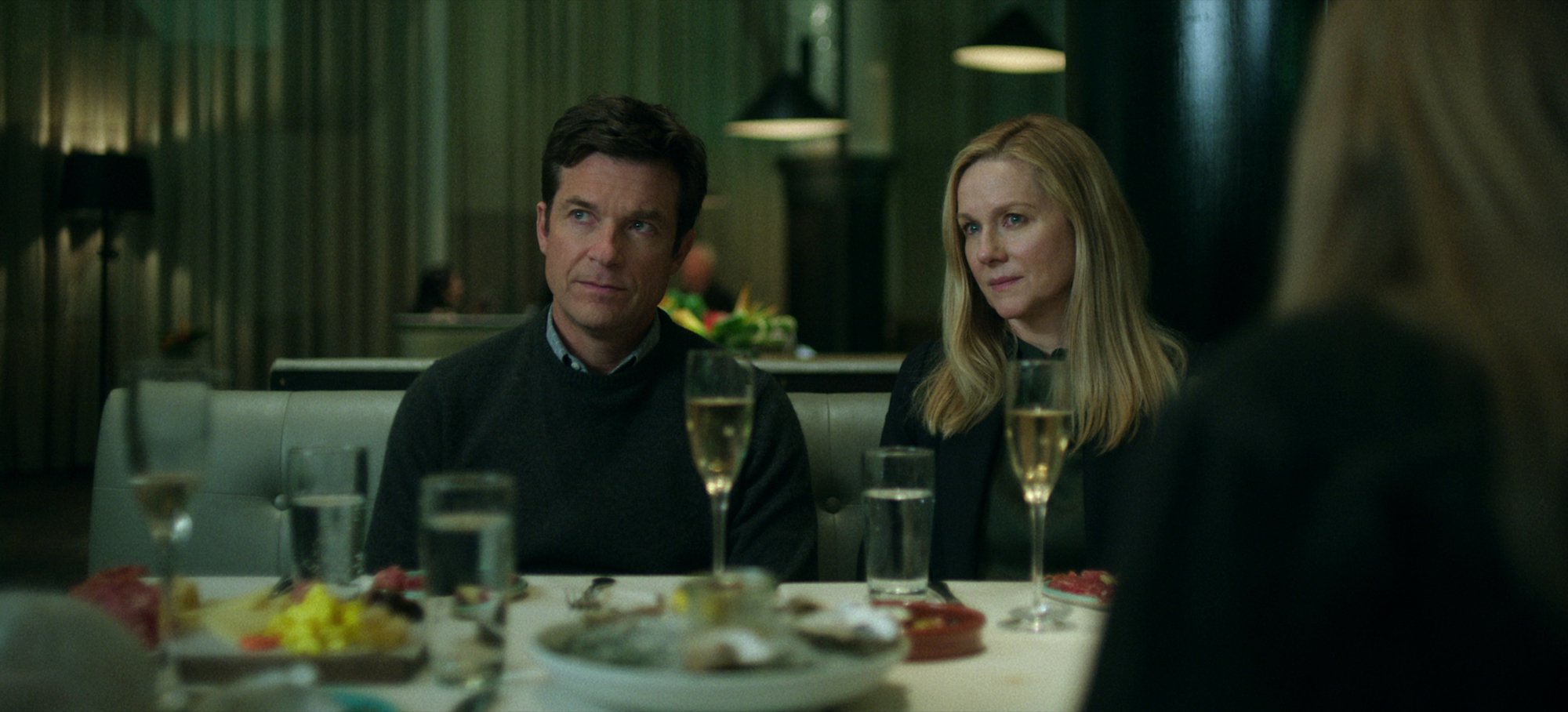 'Ozark' Season 4 Part 1 production still of Jason Bateman as Marty Byrde and Laura Linney as Wendy Byrde sitting at a table in a restaurant.