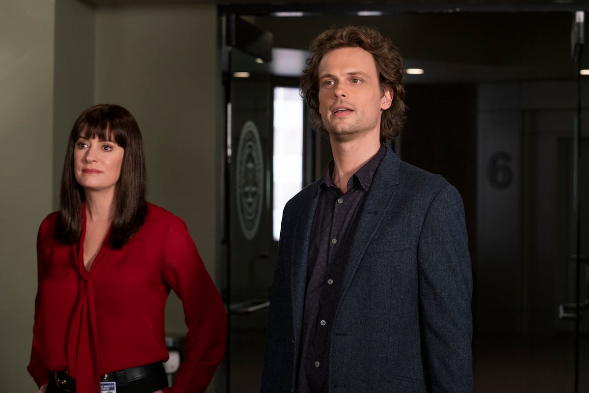 Prentiss, in red blouse, standing next to Reid, wearing dark jacket, in episode of 'Criminal Minds'