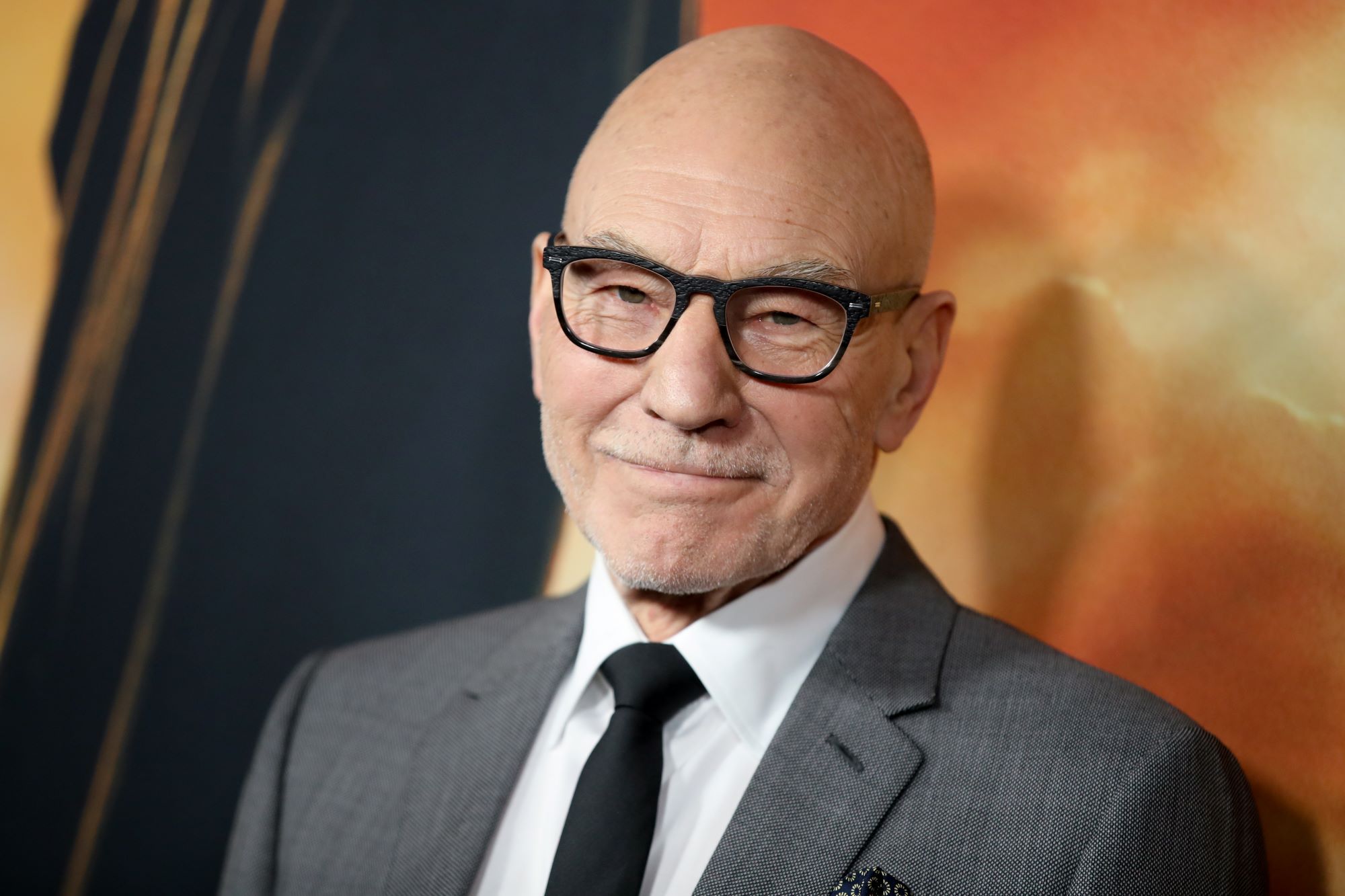 Patrick Stewart, who might be heard in the 'Doctor Strange 2' trailer, wears a gray suit over a white button-up shirt and black tie, and he wears black-framed glasses.