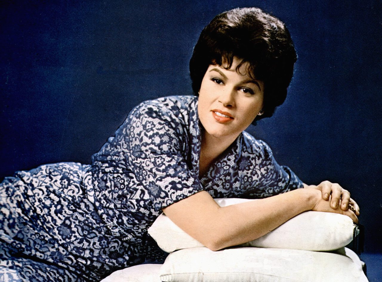 Patsy Cline poses leaned on a stack of pillows in a blue dress