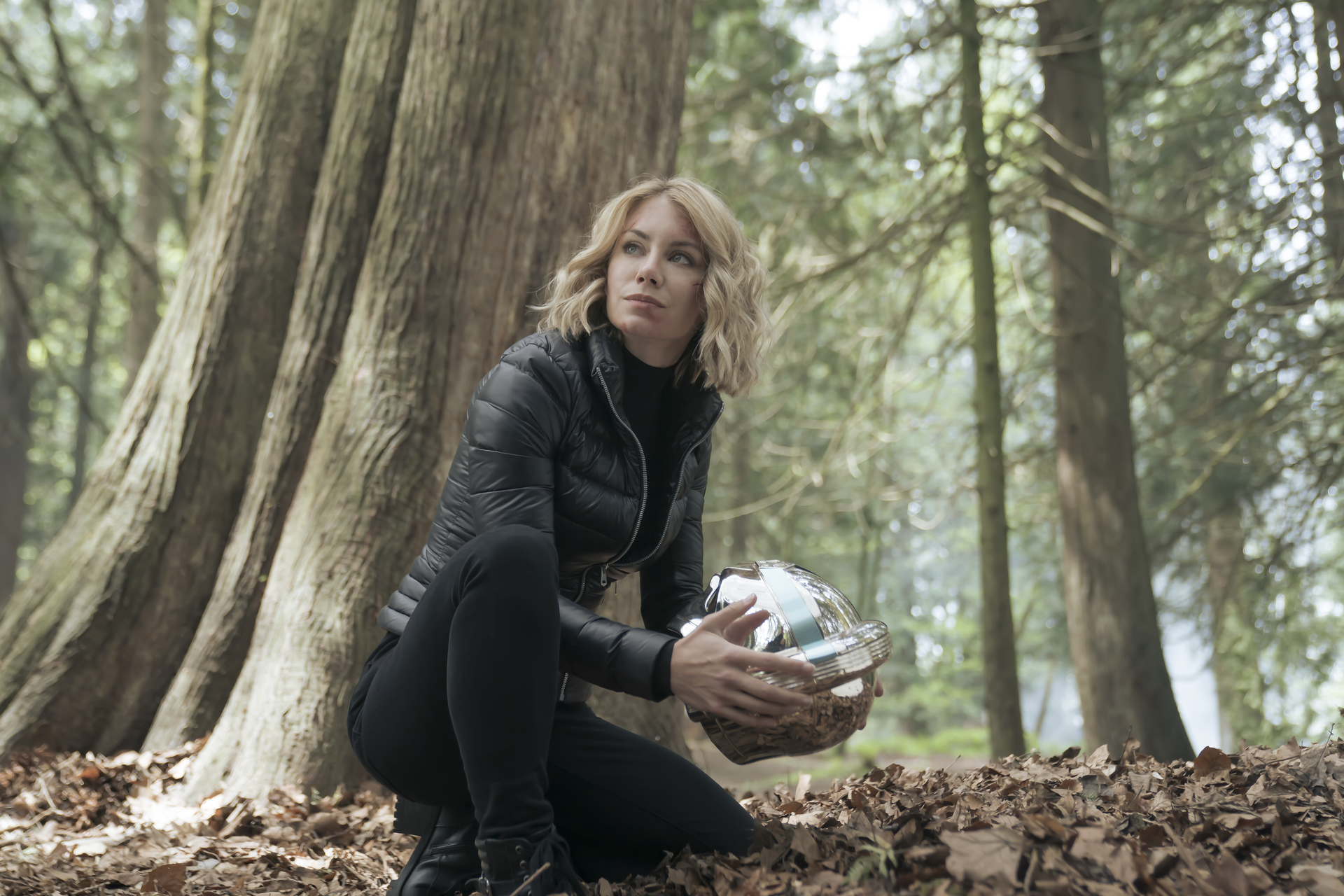 Jennifer Holland as Emilia Harcourt in 'Peacemaker' Episode 8. She's holding a helmet and kneeling.