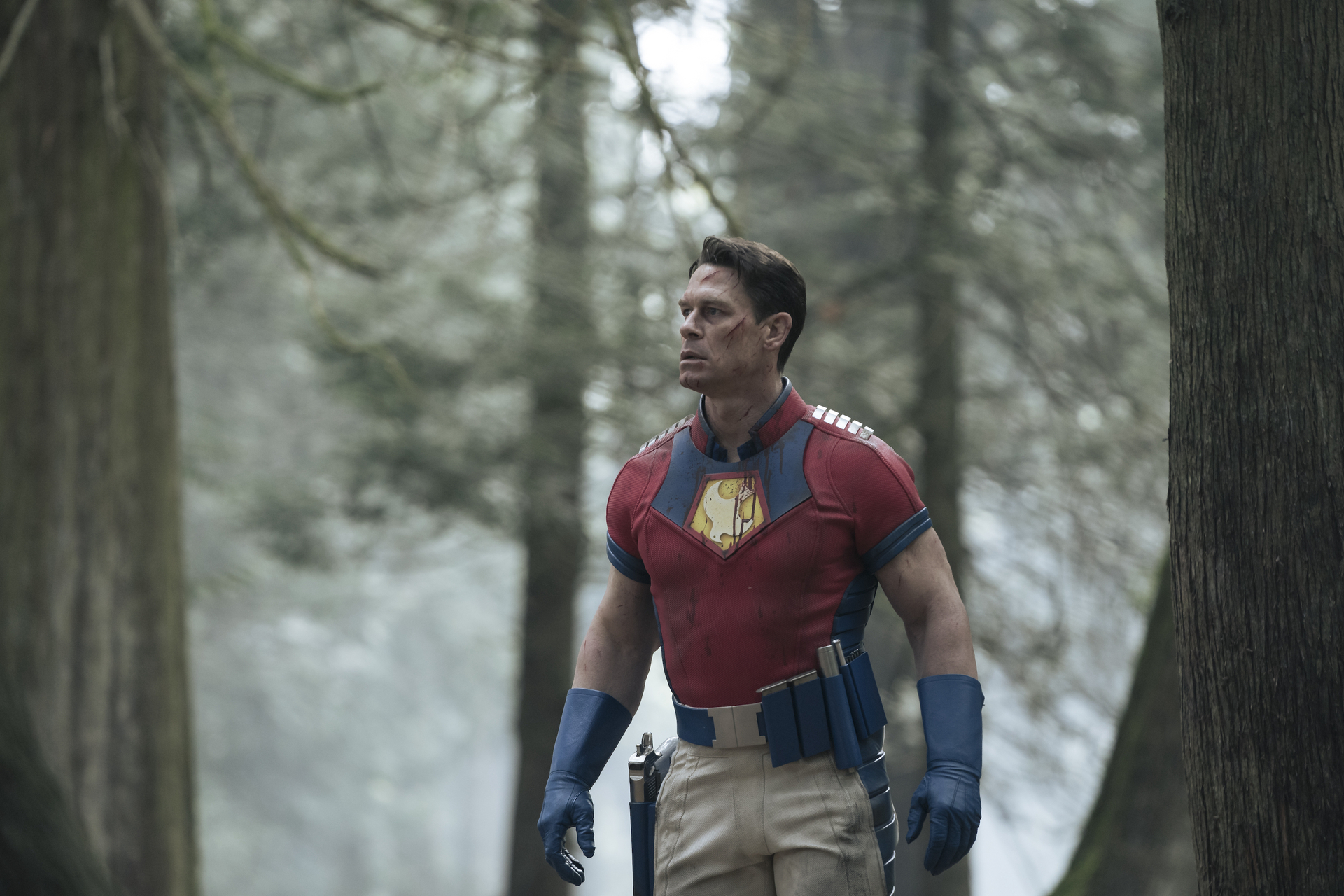 John Cena as Christopher Smith in DC's 'Peacemaker' Episode 8. He's standing in the woods and looks surprised.