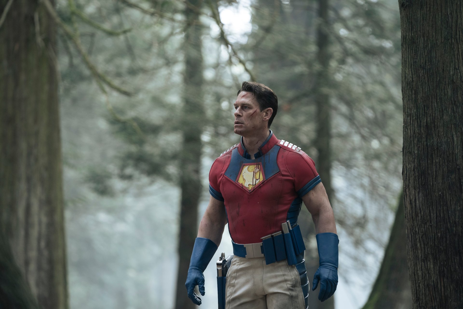 John Cena as Christopher Smith in DC's 'Peacemaker' Episode 8. He's standing in the woods and looks surprised.