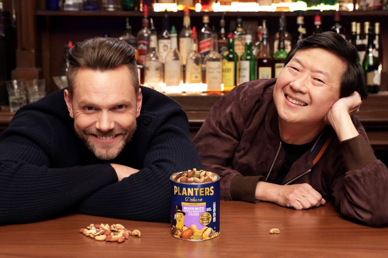 Joel McHale and Ken Jeong smiles behind a can of Planters Mixed Nuts in a production still from their upcoming Super Bowl LVI commercial