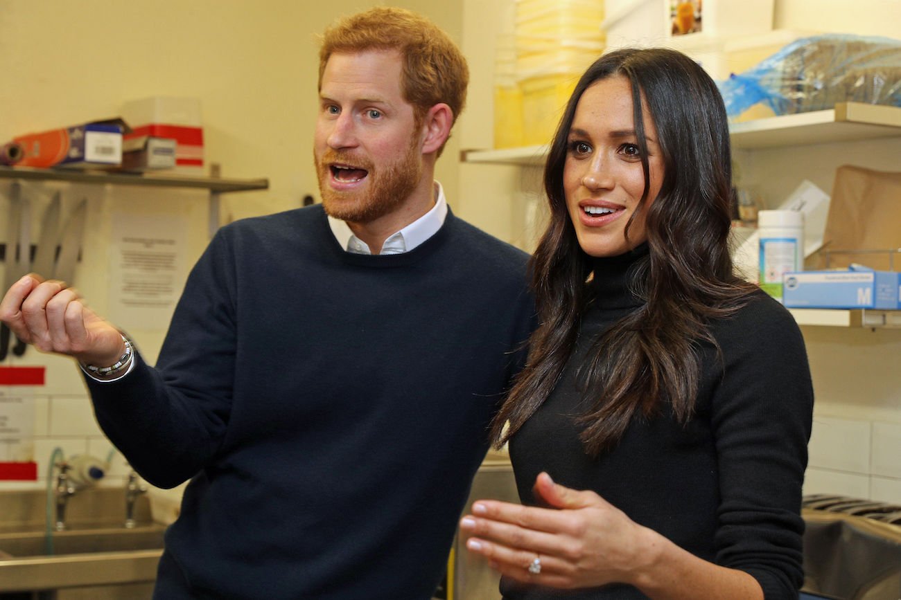 Prince Harry and Meghan Markle wearing dark outfits and talking