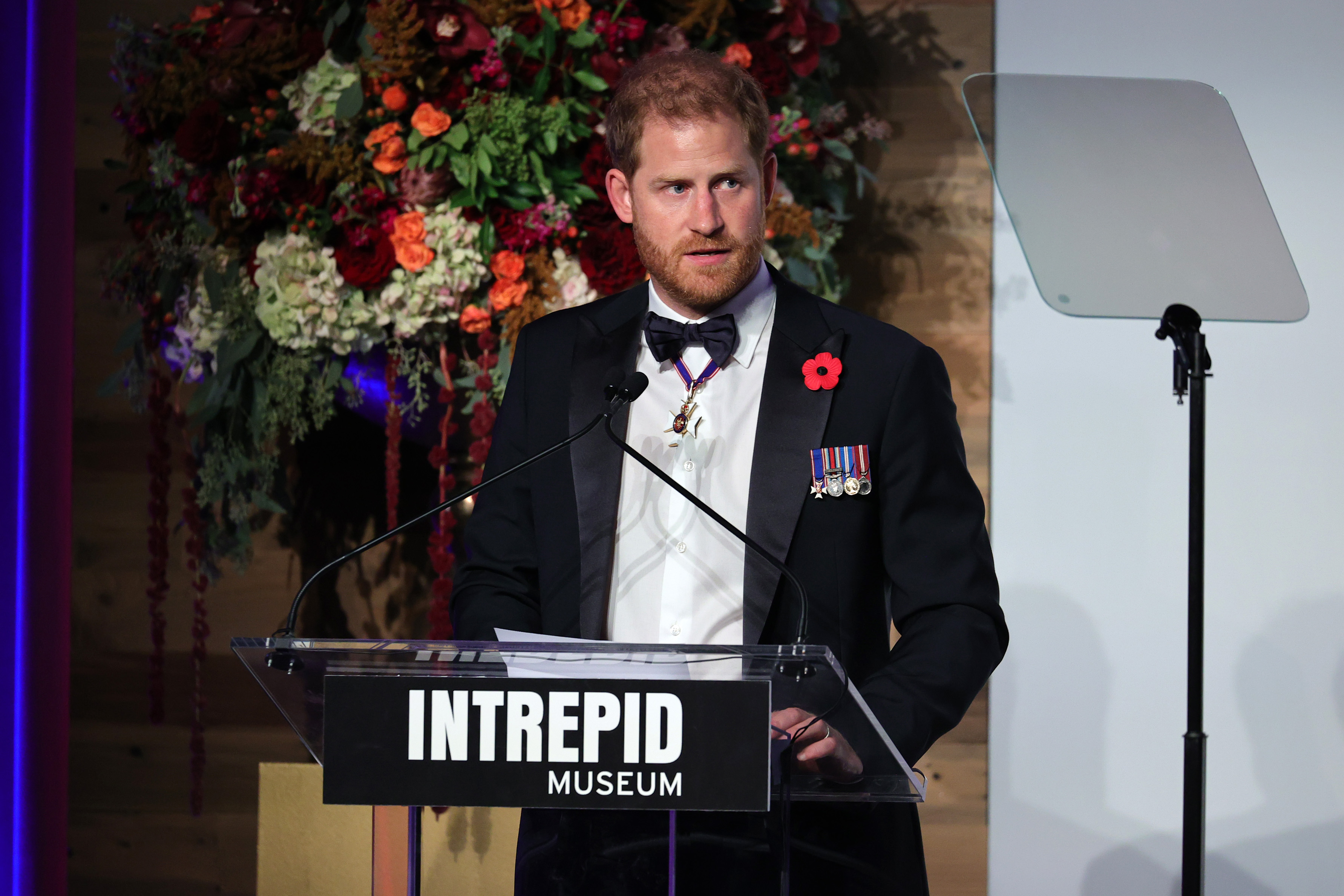 Prince Harry dressed in a tuxedo and speaking on stage at the Intrepid Museum