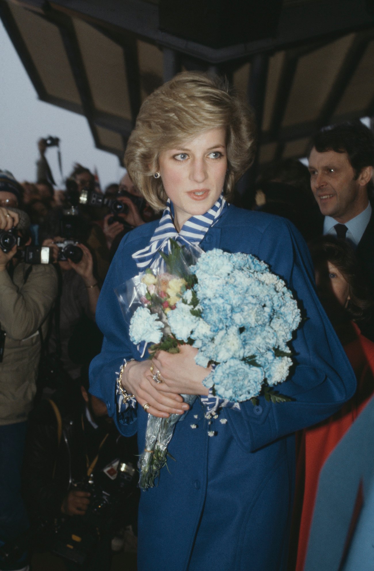 Princess Diana wearing a teal jacket and holding flowers with a crowd in the background