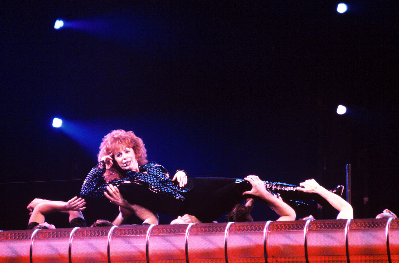 Reba McEntire performs while being held by dancers during a concert in 1995