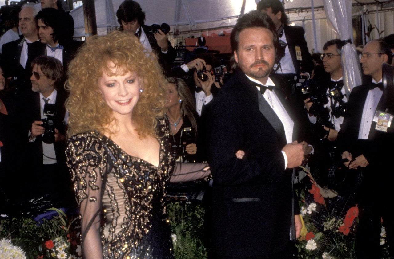 Reba McEntire in a black and gold dress walking arm in arm with Narvel Blackstock in a tuxedo c. 1991