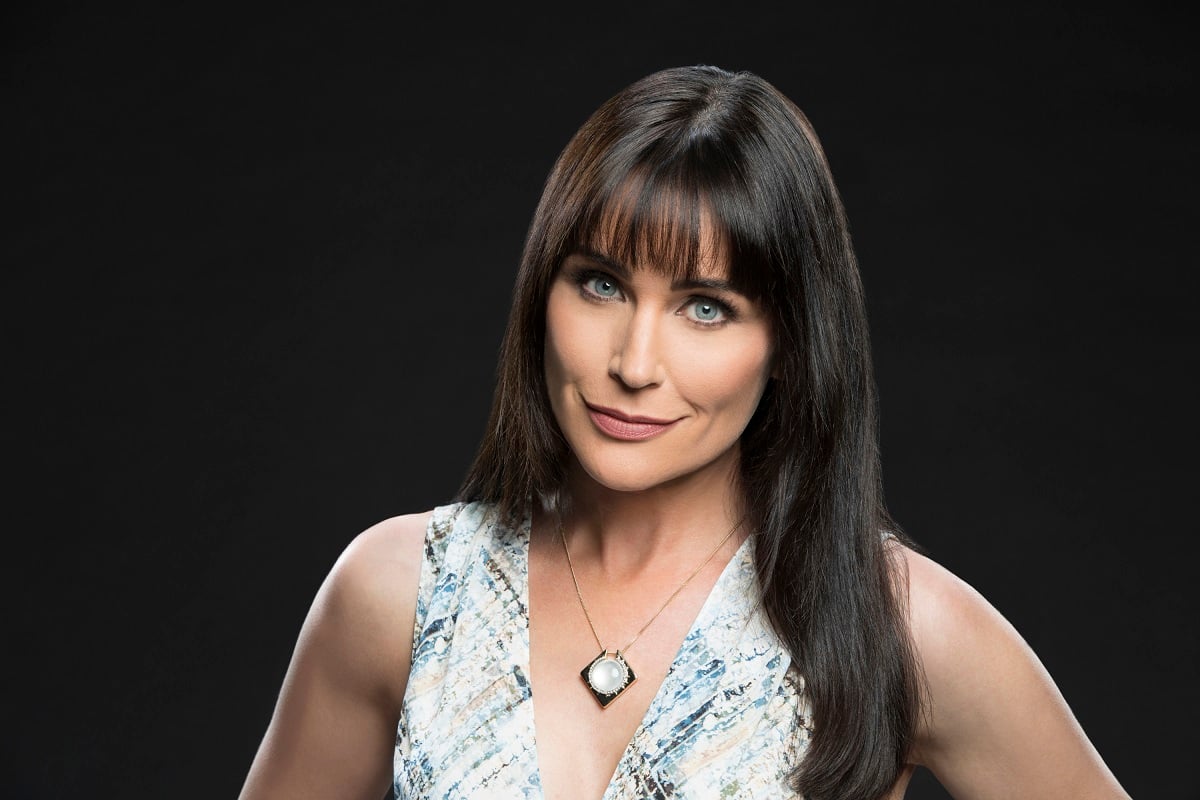 'The Bold and the Beautiful' actor Rena Sofer wearing a blue and white print dress, and standing in front of a black backdrop.