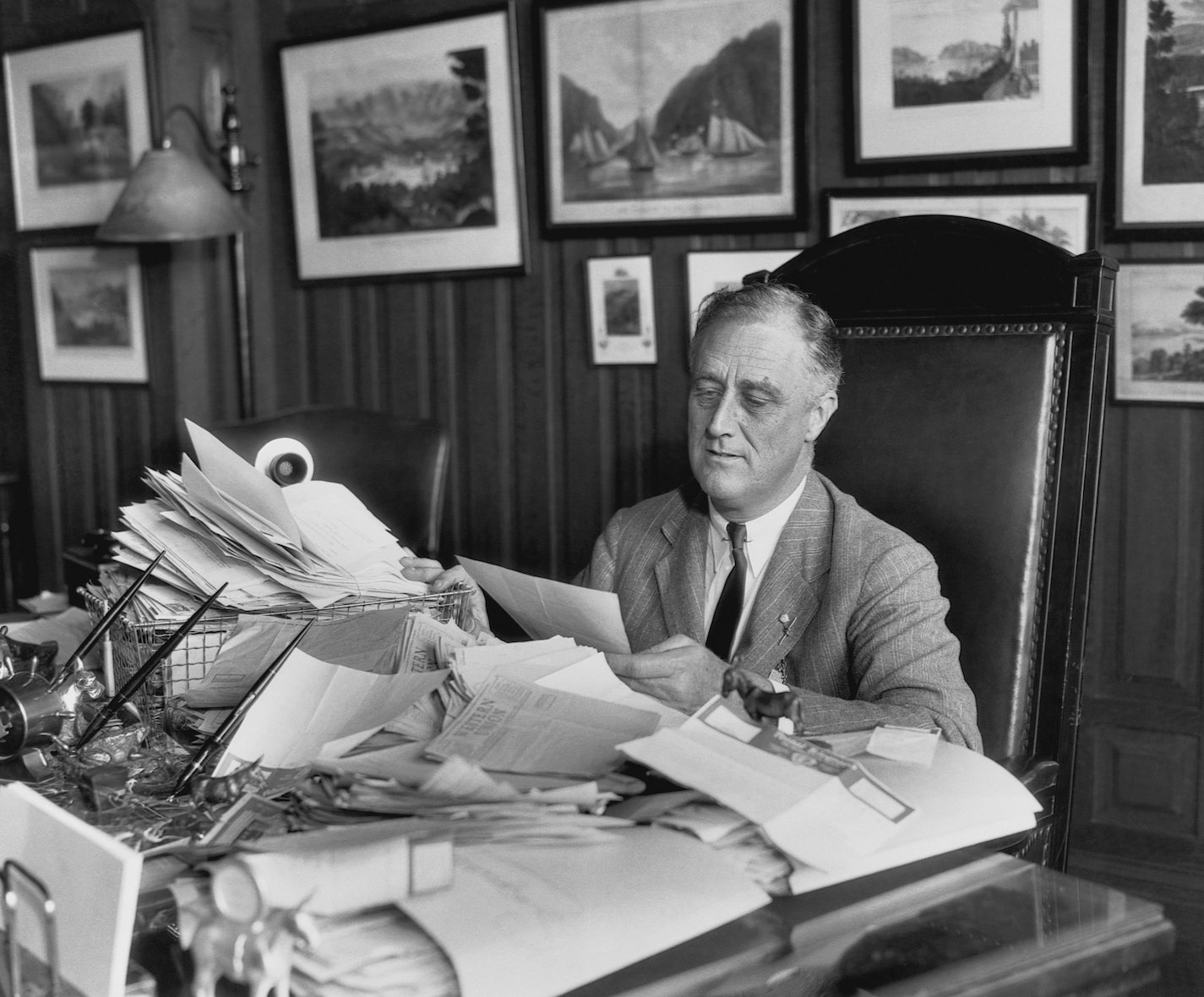A black and white photo of president Franklin D. Roosevelt in 1932 sitting at a desk piled high with letters after the election