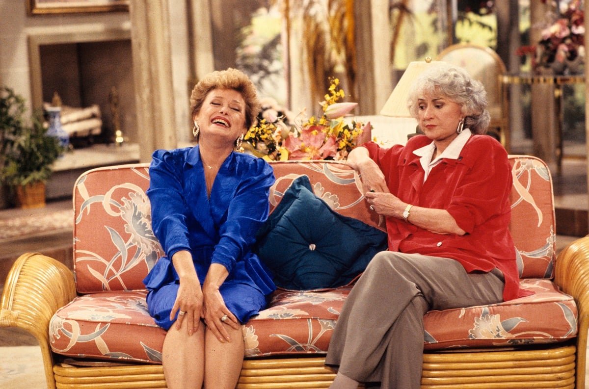 'The Golden Girls' star Rue McClanahan in a blue dress, and Bea Arthur in a red blouse and tan slacks sitting in the living room set.