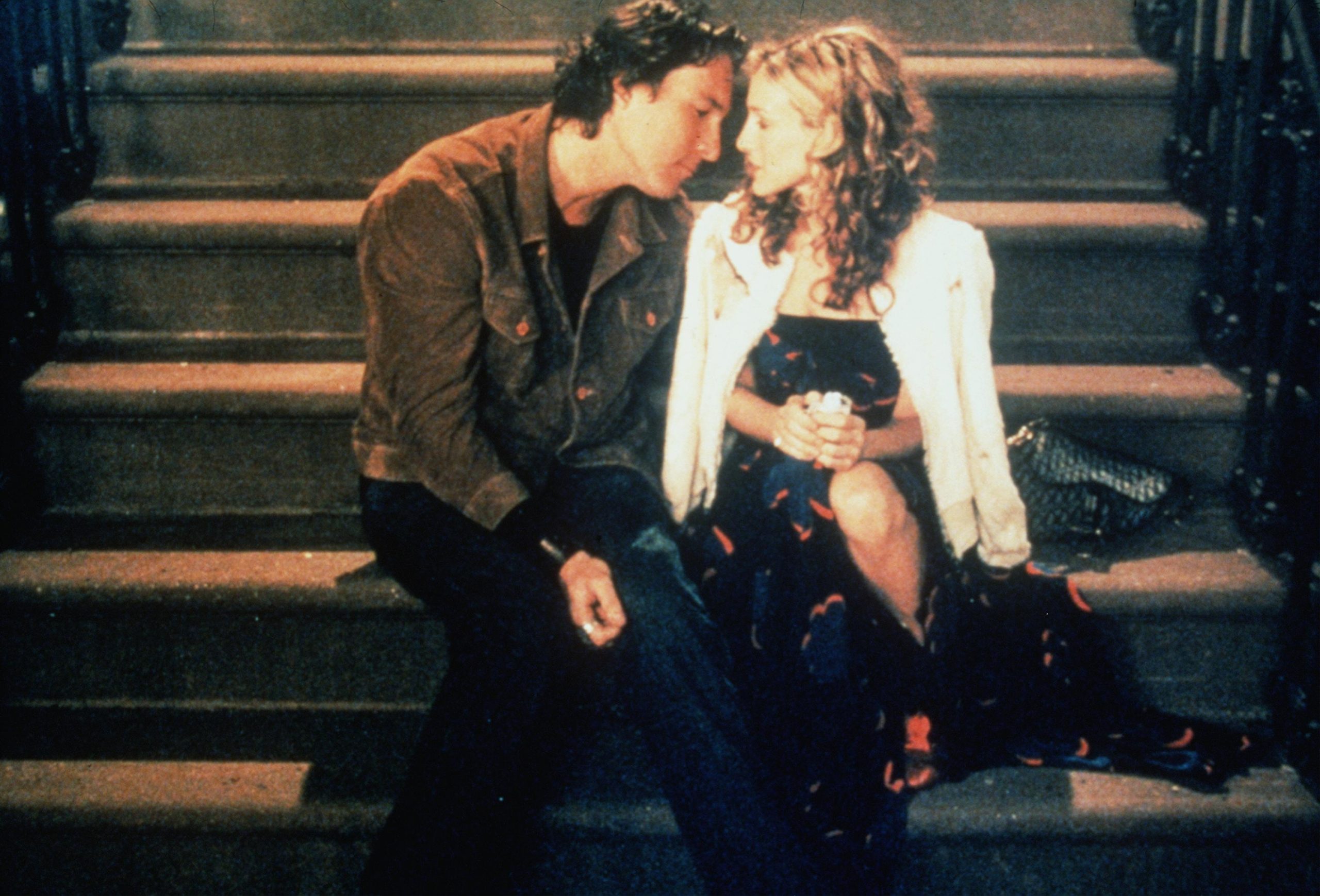 John Corbett as Aidan Shaw and Sarah Jessica Parker as Carrie Bradshaw sit on the steps of her apartment in 'Sex and the City'