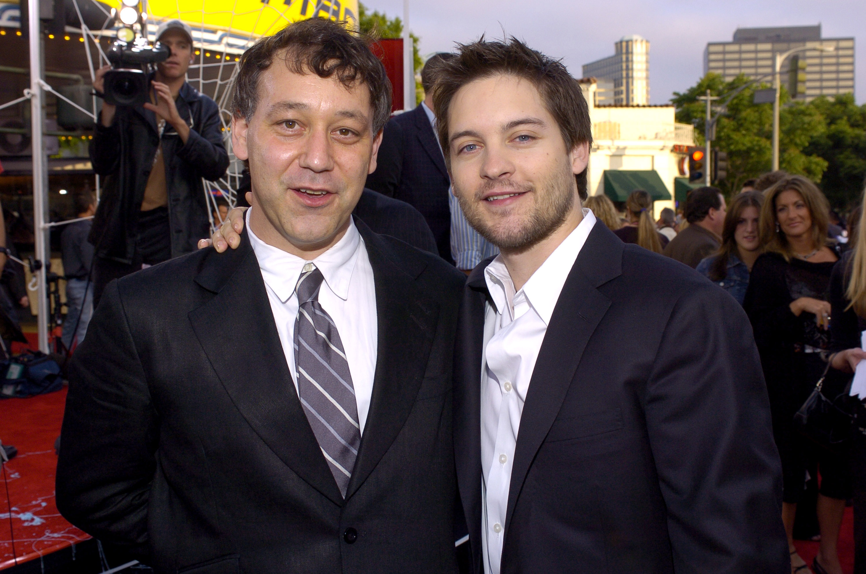 'Spider-Man' 2 director Sam Raimi and the film's star Tobey Maguire pose for pictures together on the red carpet for the premiere. Raimi wears a black suit over a white button-up shirt and a gray and white striped tie. Maguire wears a black suit over a white button-up shirt.
