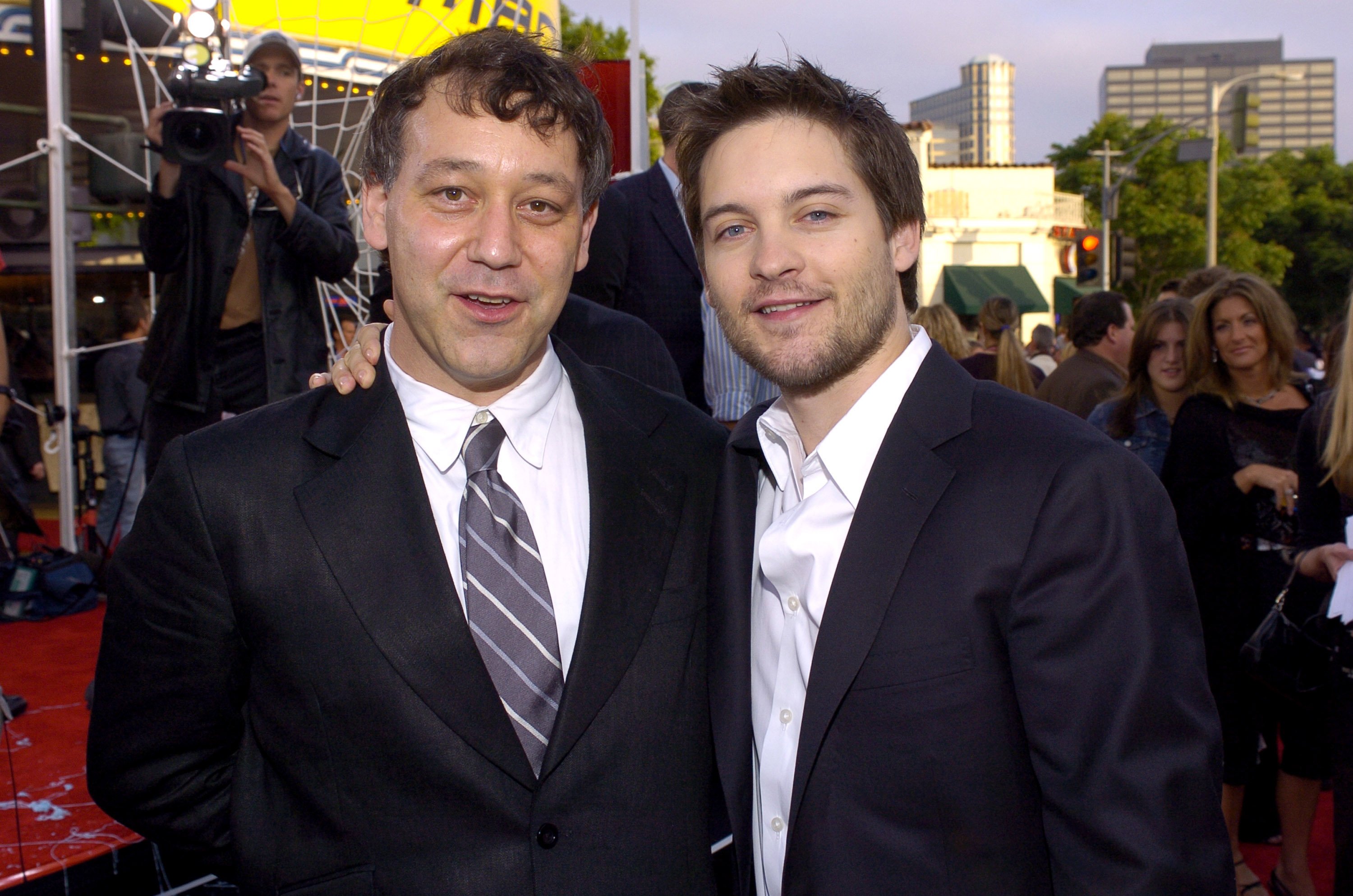'Spider-Man' 2 director Sam Raimi and the film's star Tobey Maguire pose for pictures together on the red carpet for the premiere. Raimi wears a black suit over a white button-up shirt and a gray and white striped tie. Maguire wears a black suit over a white button-up shirt.